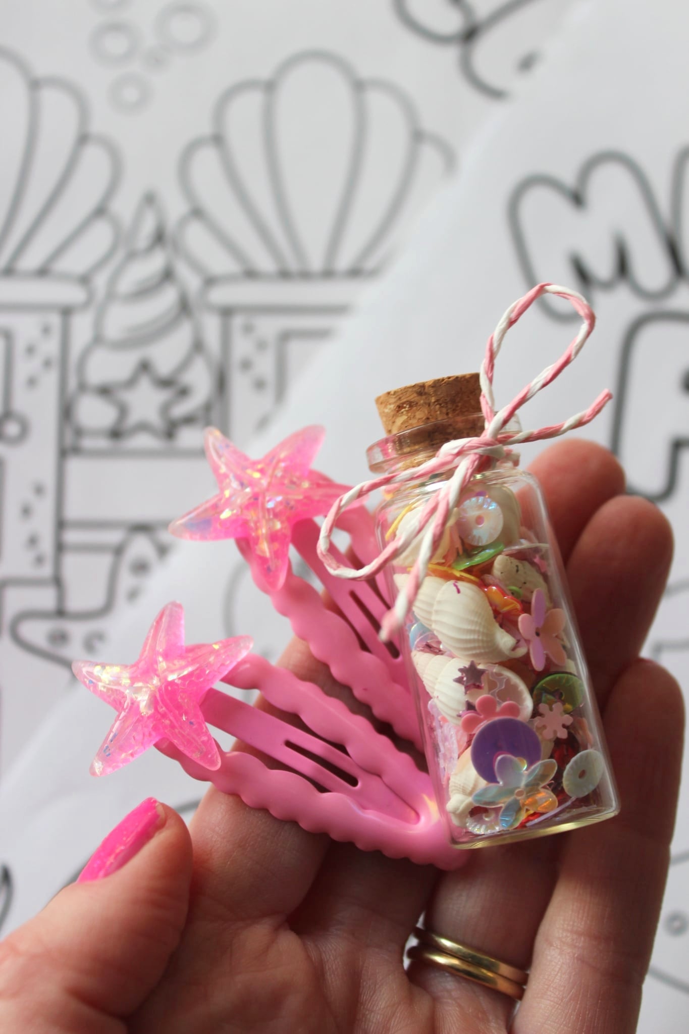 Small bottle with decorative items and pink star-shaped clips held by a hand.